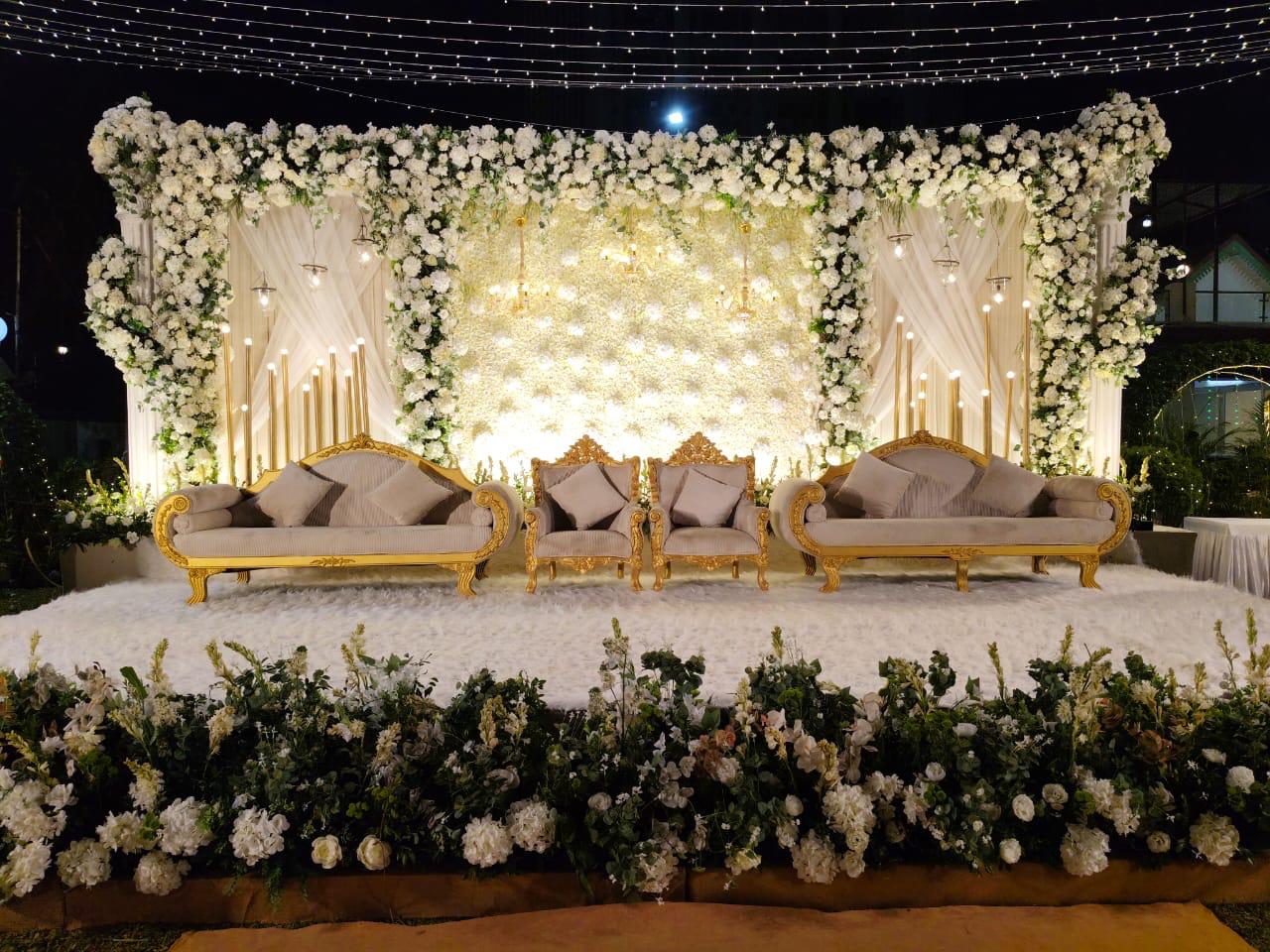 Luxury wedding stage with lush white floral canopy, golden seating and fairy light backdrop at Nariman Point Lawn